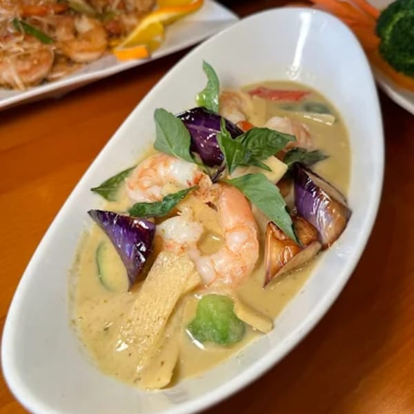 Thai green curry with shrimp, eggplant, and bamboo shoots in a white bowl.