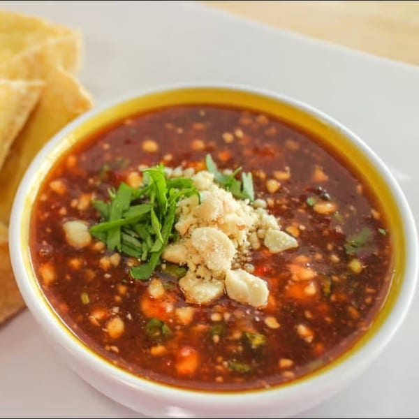Close-up of a bowl of Thai peanut sauce, garnished with crushed peanuts and fresh herbs.