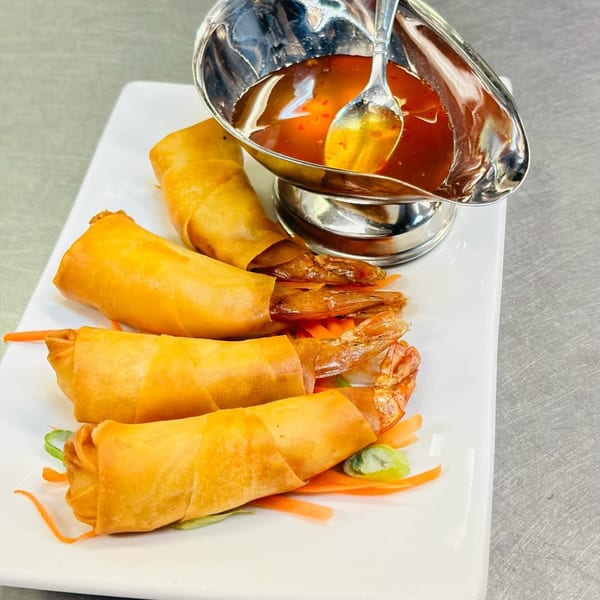Golden fried shrimp spring rolls with sweet chili dipping sauce on a white rectangular plate.