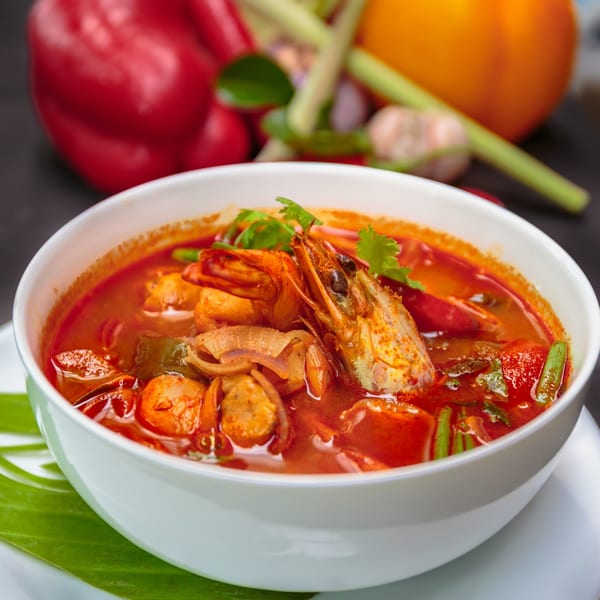 A vibrant bowl of Thai Tom Yum soup with shrimp, mushrooms, and herbs, on a banana leaf.