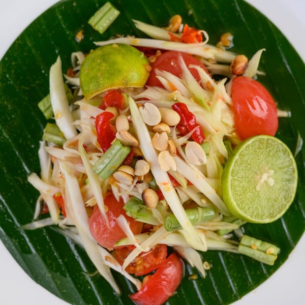 Close-up of a vibrant Thai papaya salad with peanuts, tomatoes, and lime on a banana leaf.